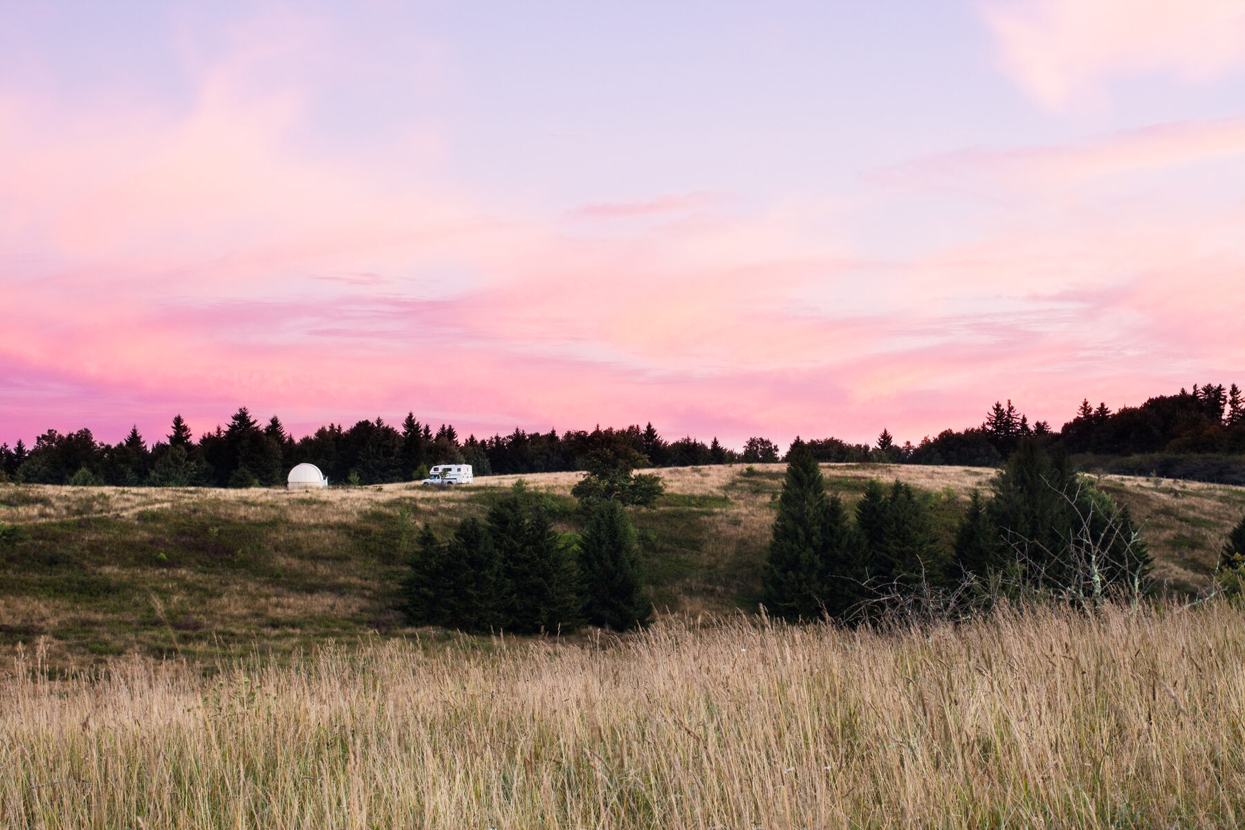 Pink sunset sky over the Spruce Knob Mountain Center campsite, with the observatory dome and RVs visible on the field
